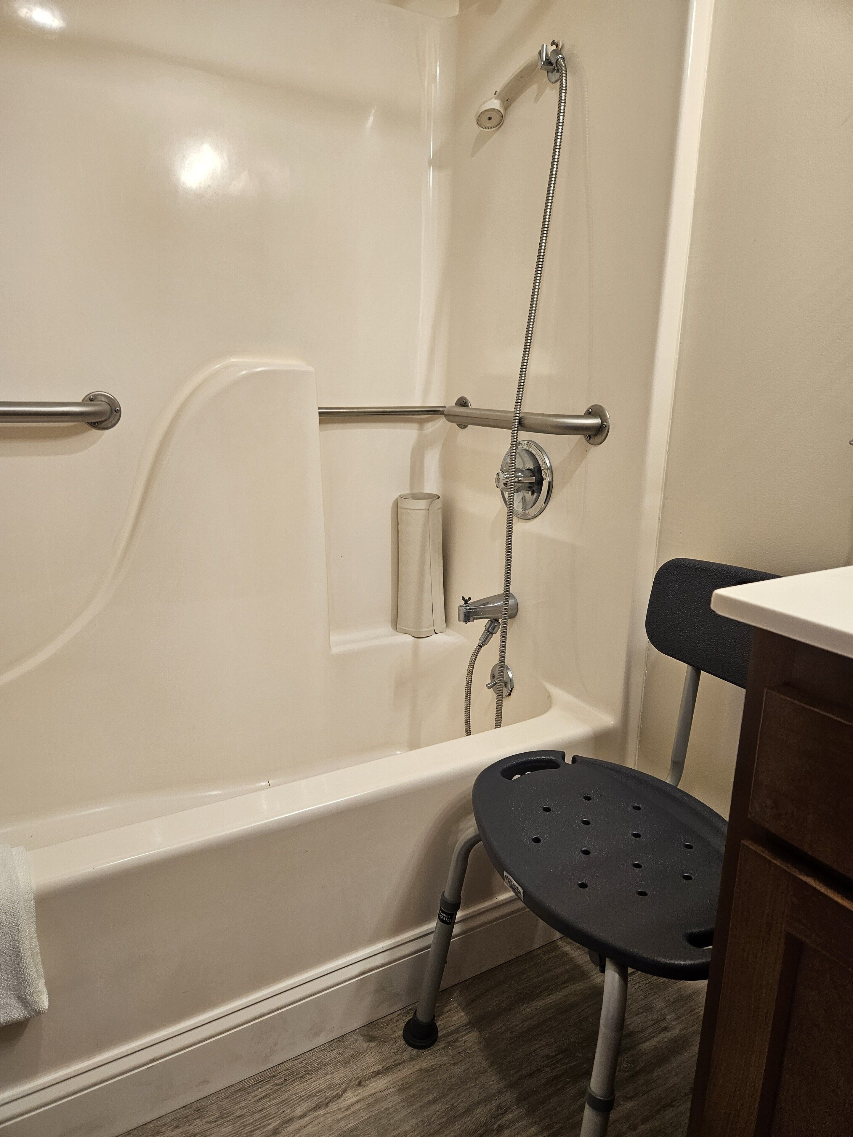 A bathroom with a bathtub, grab bars, a showerhead, and a toilet with a black seat.