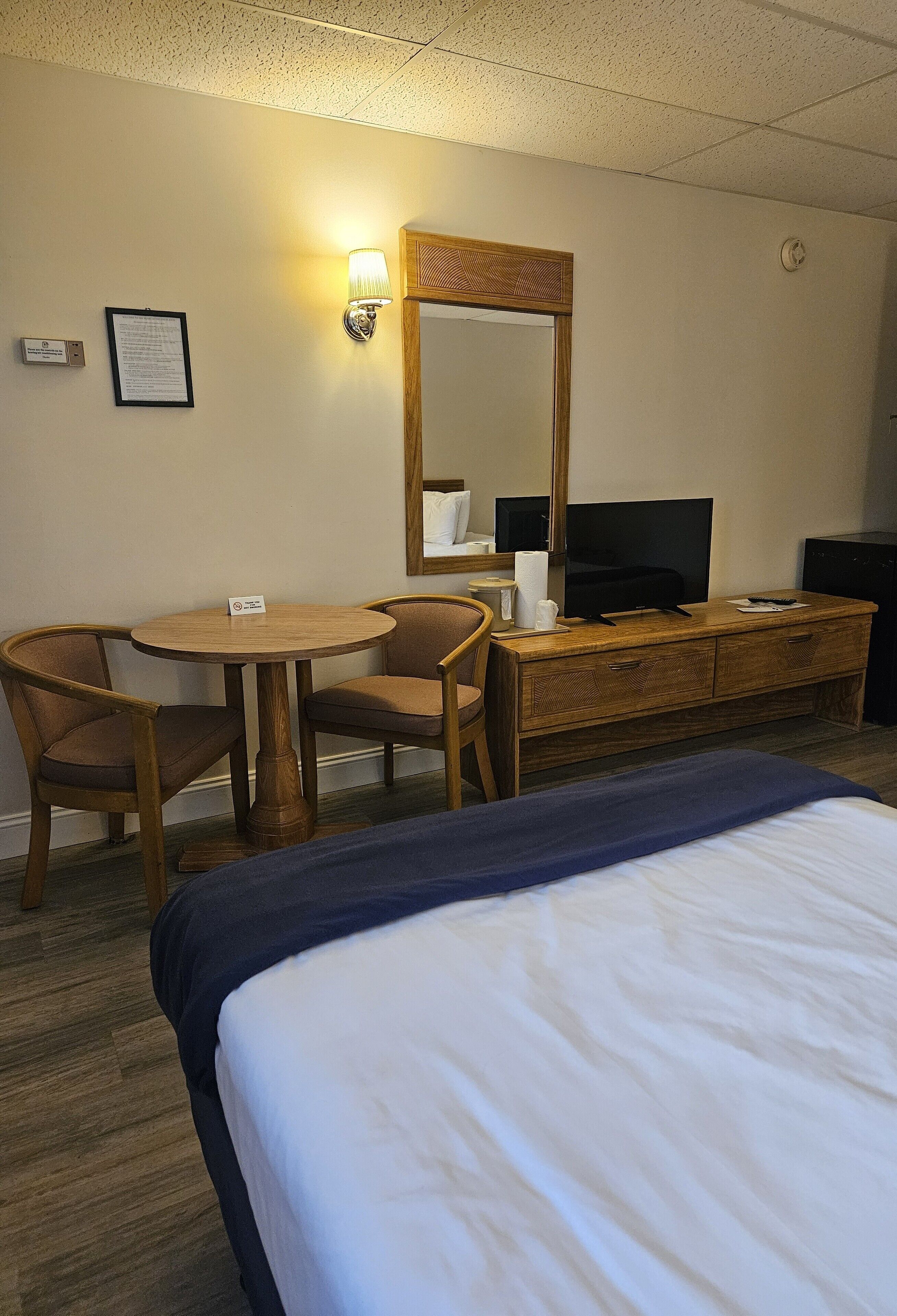 A hotel room with a bed, a desk with a chair, a television, and a mirror.