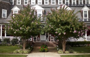 A two-story house with a front porch, a white picket fence, and a garden with flowering trees.