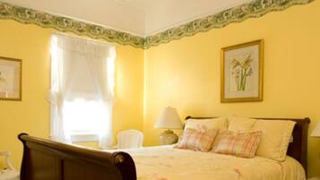 A bedroom with a bed, a chair, a lamp, and a window with curtains.