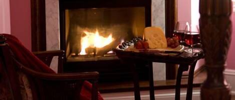 A cozy room with a fireplace, a table with food and drinks, and a chair.