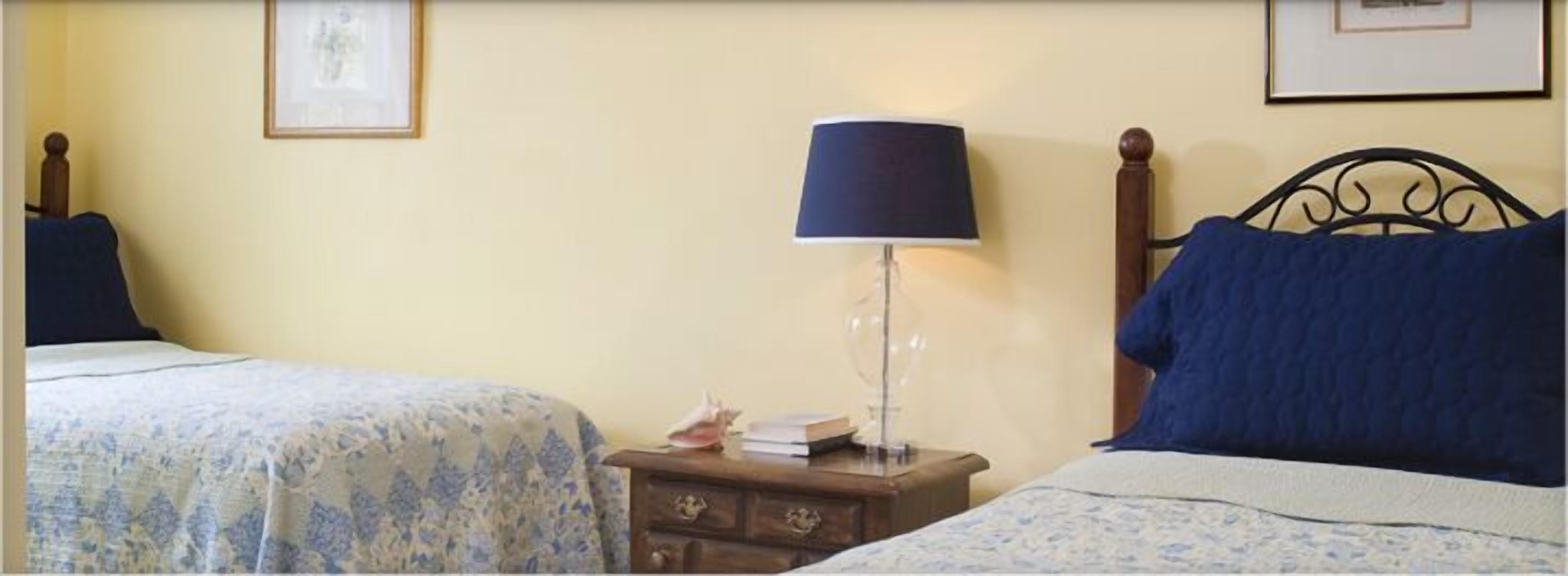 A bedroom with two beds, a nightstand with a lamp, and framed pictures on the wall.