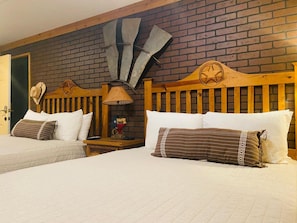 A room with two beds, wooden headboards, a brick wall, and a Texas flag decoration. - Big Texan Motel (Amarillo)