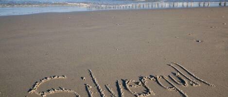 A beach with the word "Silver" written in the sand, a pier in the background, and waves approaching the shore.