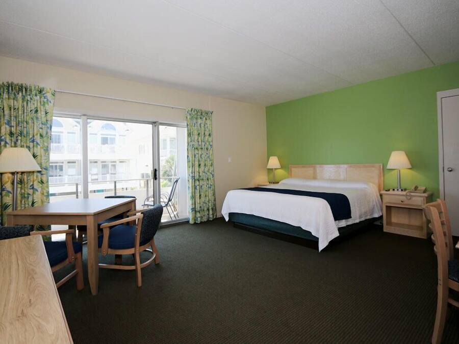 Une chambre d’hôtel comprenant un lit, un bureau, deux chaises, une table et un balcon avec des rideaux.