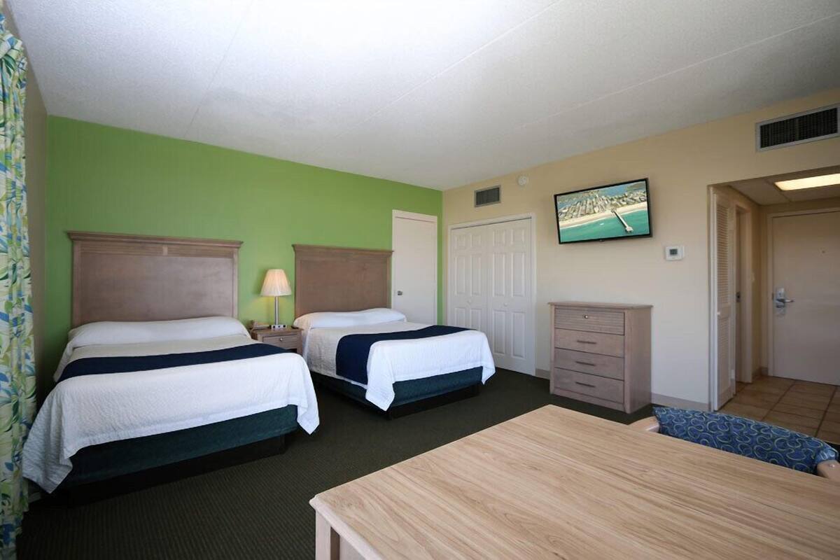 Ein Hotelzimmer mit zwei Betten, einem Schreibtisch, einem Schminktisch und einem an der Wand befestigten Fernseher.