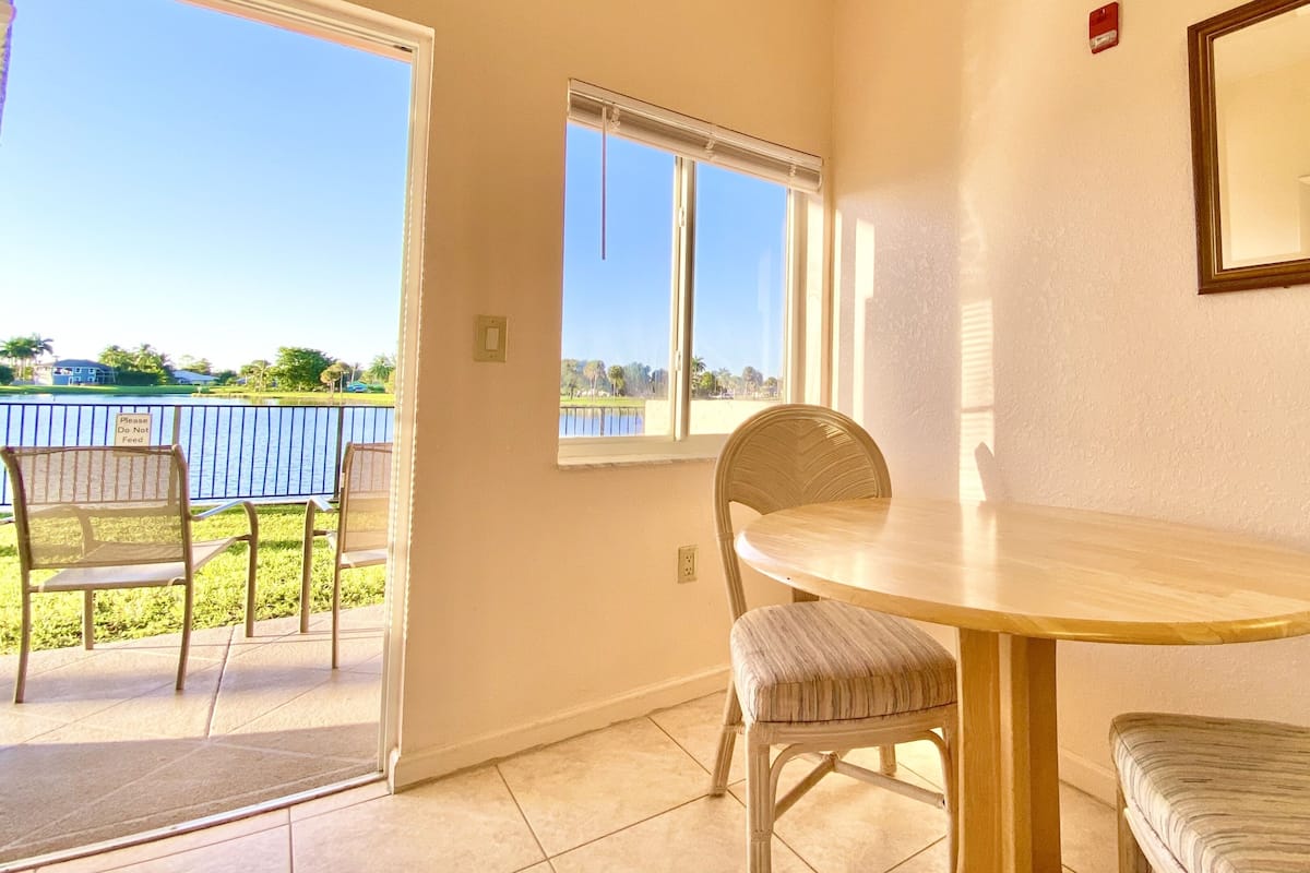 Una habitación con una mesa de comedor y sillas, una ventana con vistas al agua y una puerta que da al exterior.