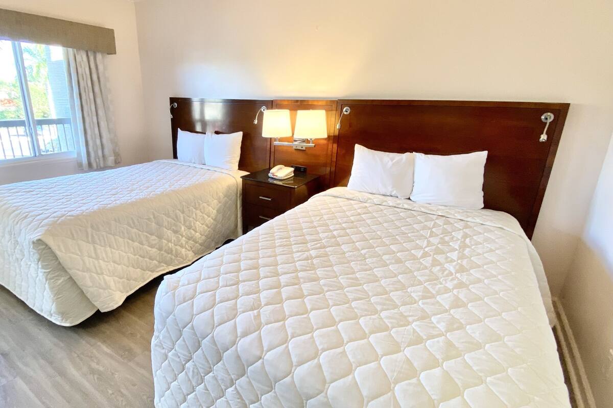 A hotel room with two beds, a nightstand with a lamp, and a window with curtains.