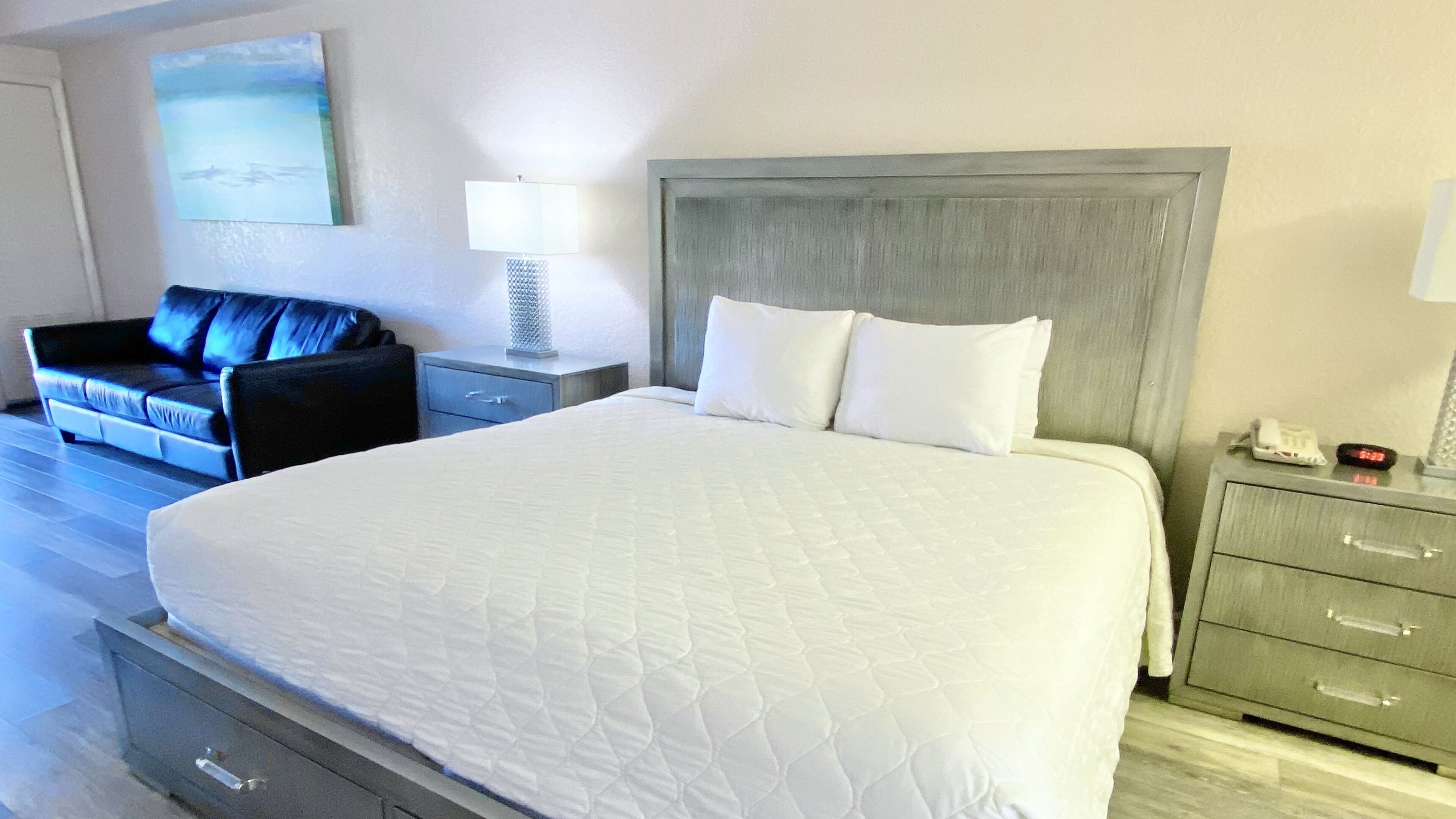 A hotel room with a large bed, a nightstand with a lamp, a sofa, and a painting on the wall.