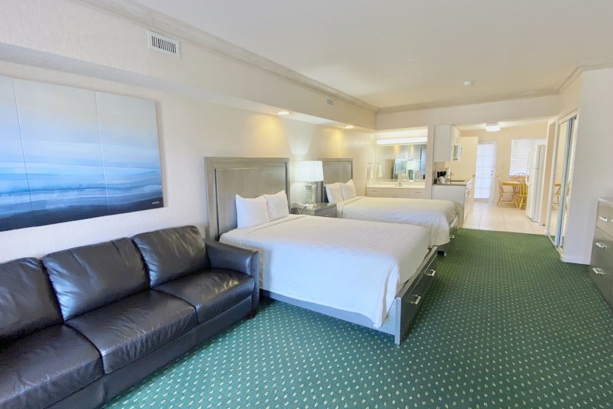 Una habitación de hotel con una cama grande, una cama más pequeña, un sofá y una alfombra verde.