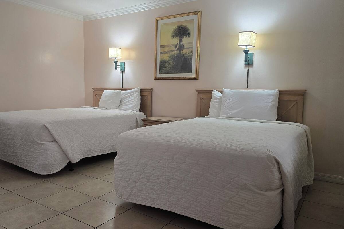 Two single beds with white bedding, a wooden chair, and a painting on the wall.