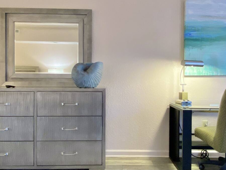 A grey dresser with drawers, a mirror above it, and a painting on the wall.