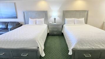 Ein Hotelzimmer mit zwei Betten, einem Nachttisch mit Lampe, einem Sessel und einem grünen Teppich mit Muster.