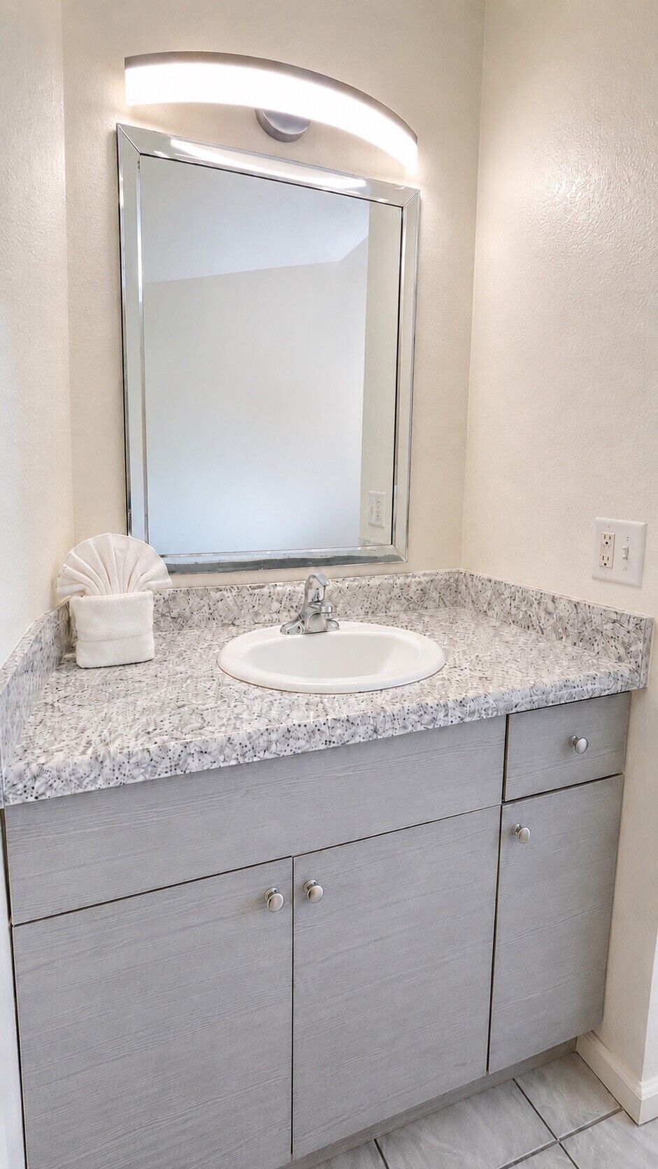 Un baño con encimera de granito, un lavabo blanco, un espejo grande y una toalla.