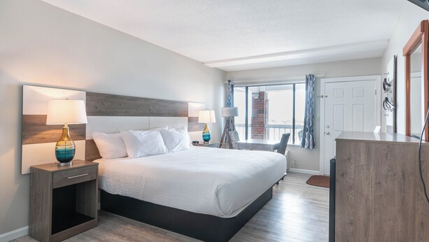 A modern hotel room with a large bed, bedside tables with lamps, a desk, and a view of the city through the window. - The Anchorage Inn and Marina (Ocracoke)