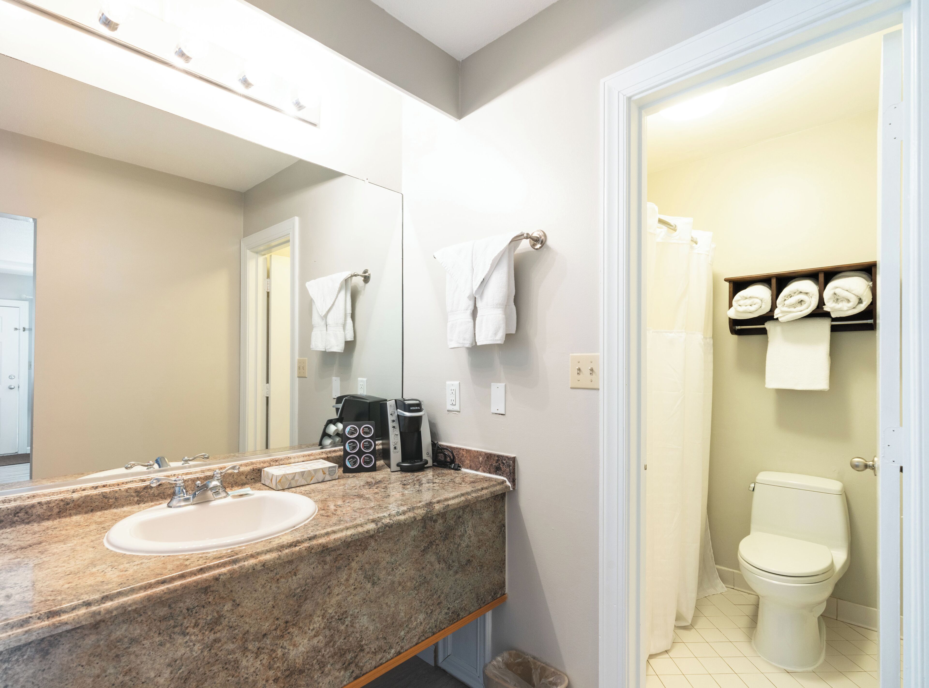 Une salle de bain dotée d’un comptoir en granit, d’une machine à café, de toilettes et d’un porte-serviettes avec des serviettes pliées.