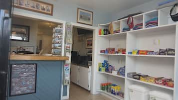 A room with a reception desk, a bulletin board with various signs, and shelves stocked with snacks and toiletries.