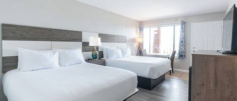 Habitación de hotel con dos camas, cabecero de madera, mesita de noche con lámpara, escritorio con televisor y ventana con cortinas.
