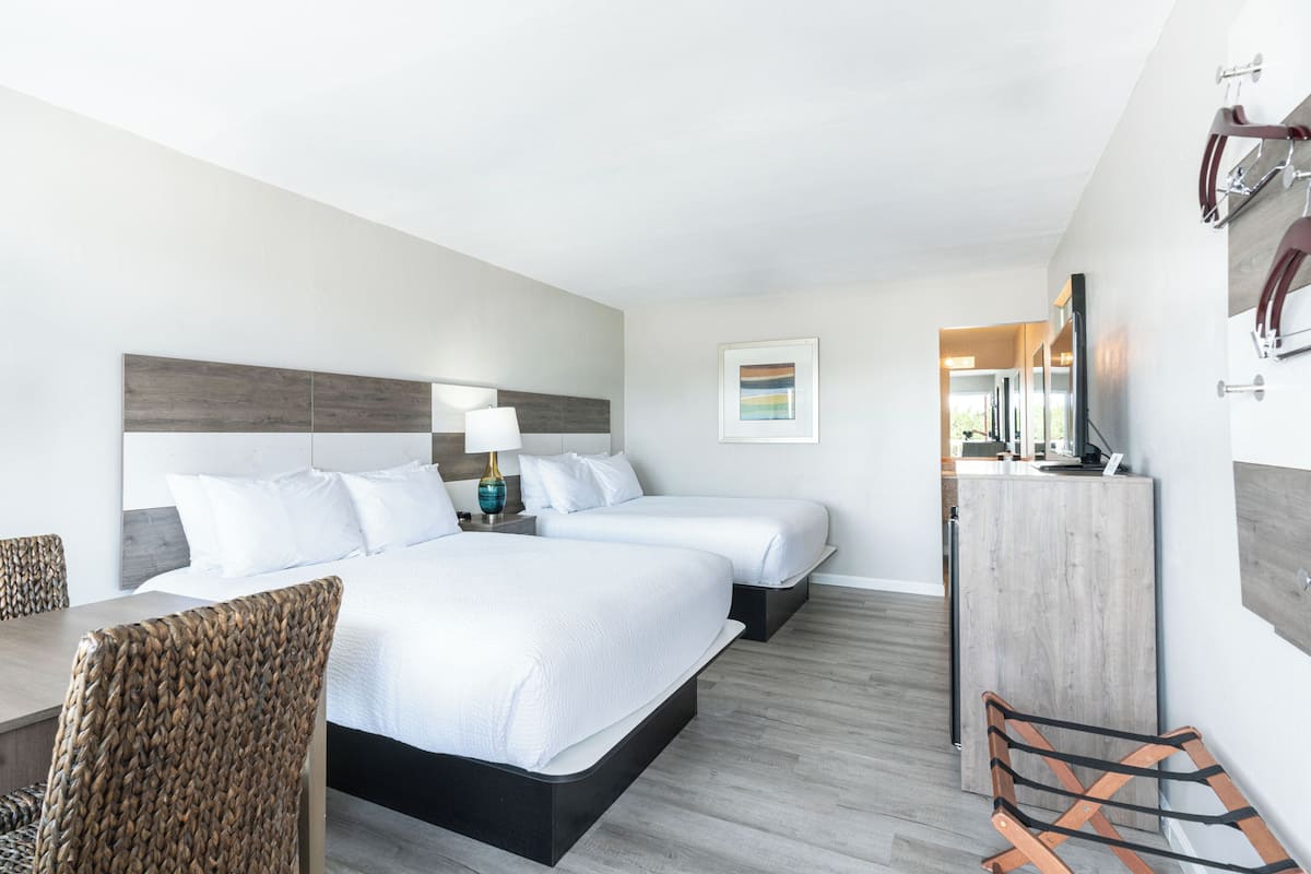 A hotel room with two beds, a desk, a chair, a dresser, and a mirror.