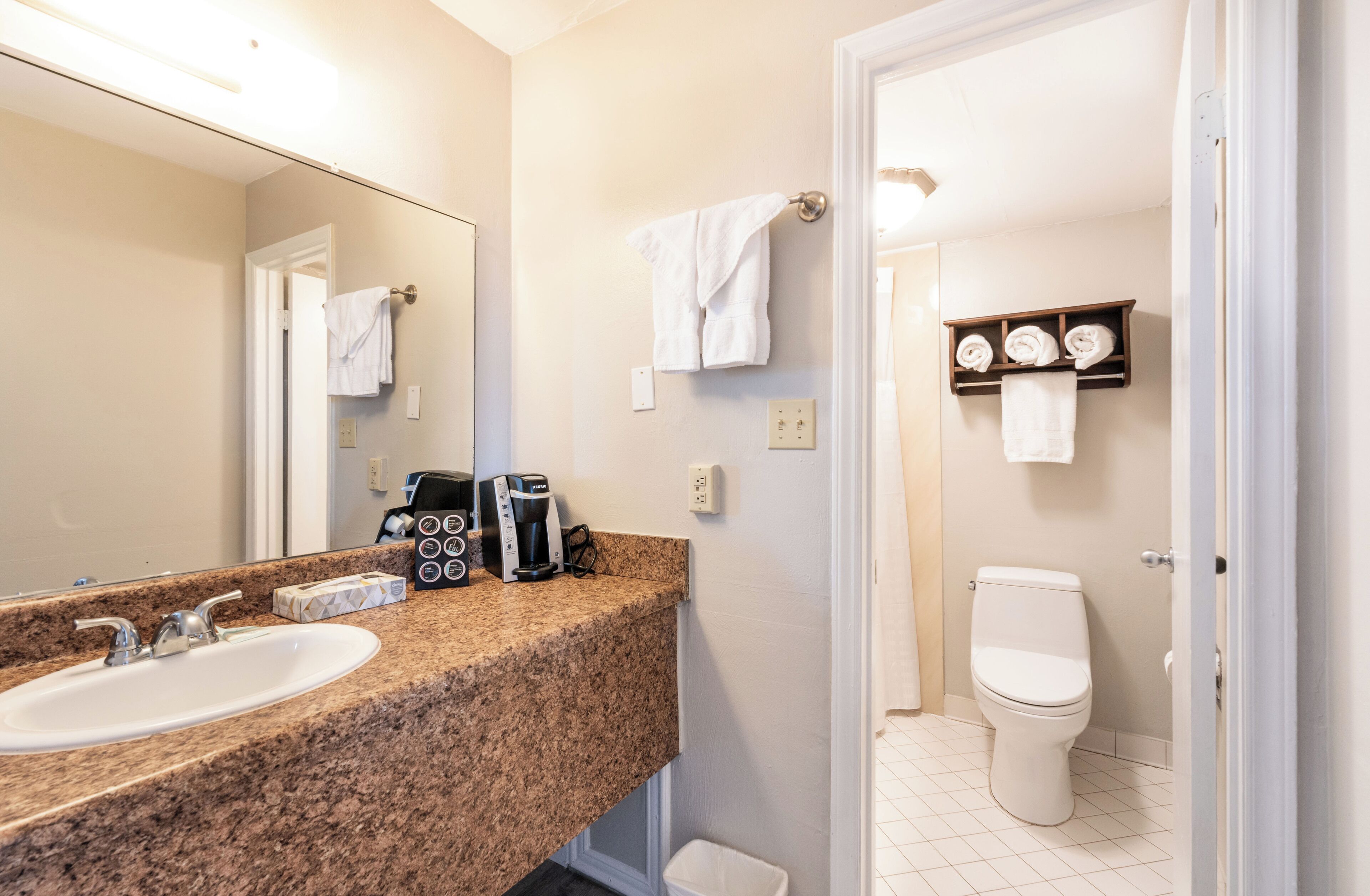 A bathroom with a granite countertop, a sink, a coffee maker, and a toilet.