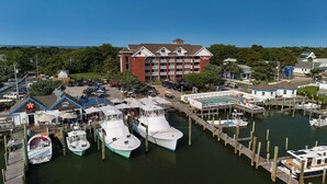 A marina with several boats docked, a hotel with a red brick facade, and a pool area with people. - The Anchorage Inn and Marina (Ocracoke)