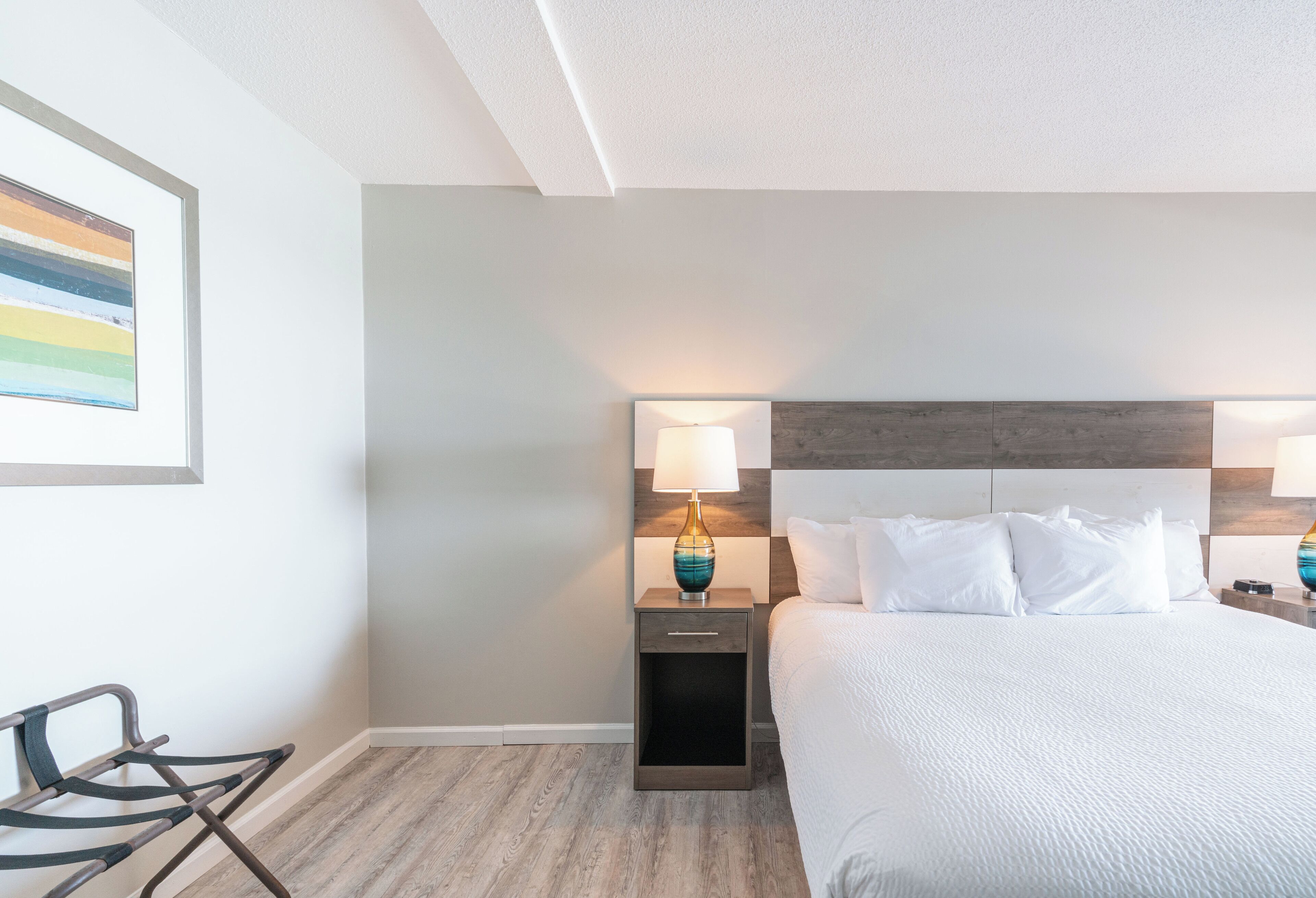 A hotel room with a bed, bedside table, lamp, and a chair.
