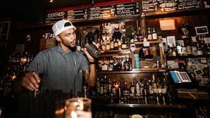 A bar with a variety of bottles and a menu board in the background. - Firehouse Hostel (Austin)