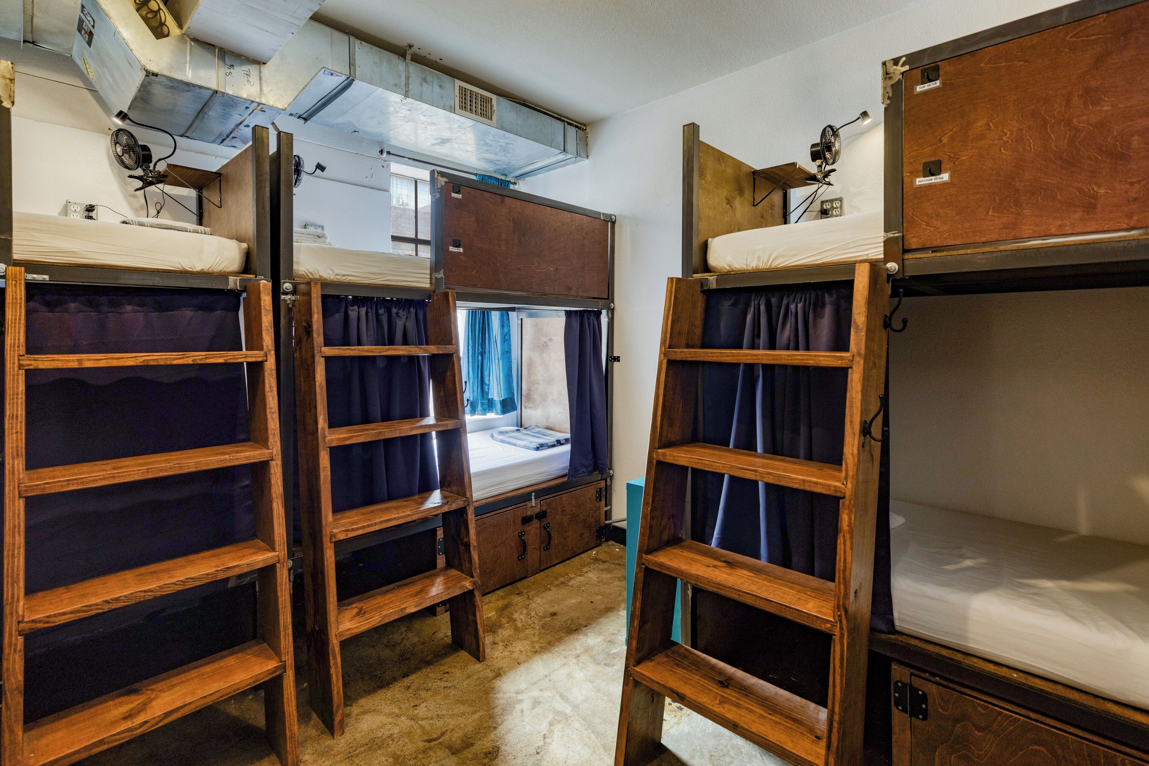 A dormitory room with bunk beds, a window with curtains, and a ceiling fan.