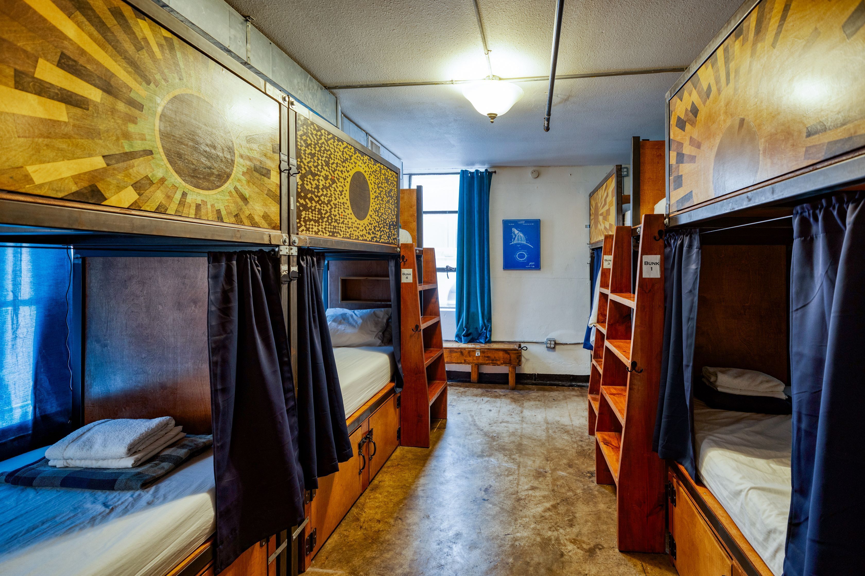 Una habitació de dormitori amb llits superposats, un terra de fusta, una finestra amb cortines i una làmpada de paret.