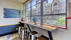A room with a large window, wooden bar stool seating, a globe on the window sill, and a map on the wall. - Firehouse Hostel (Austin)
