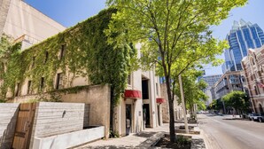 A building with a modern facade, a tree-lined sidewalk, and a clear sky. - Firehouse Hostel (Austin)