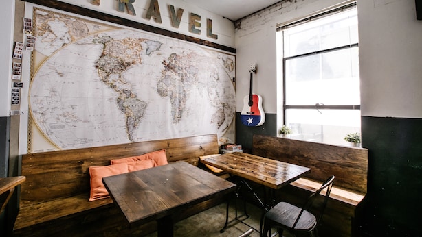 A room with a large world map on the wall, a guitar, wooden furniture, and a window with a view. - Firehouse Hostel (Austin)