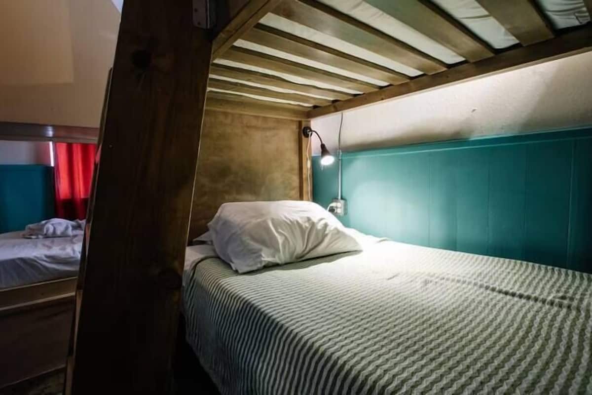 A single bed with a striped bedspread and a white pillow in a room with teal walls and wooden ceiling beams.