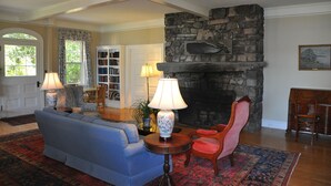 A living room with a stone fireplace, a blue sofa, a red chair, and a bookshelf. - The Claremont Hotel (Southwest Harbor)