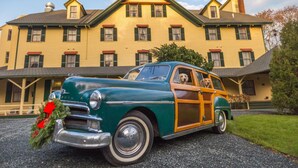 A vintage car parked in front of a large yellow building with a green roof and multiple windows. - The Claremont Hotel (Southwest Harbor)
