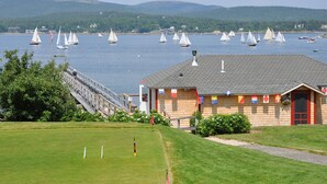 A coastal building with a grassy area in front, a dock, and sailboats on the water. - The Claremont Hotel (Southwest Harbor)