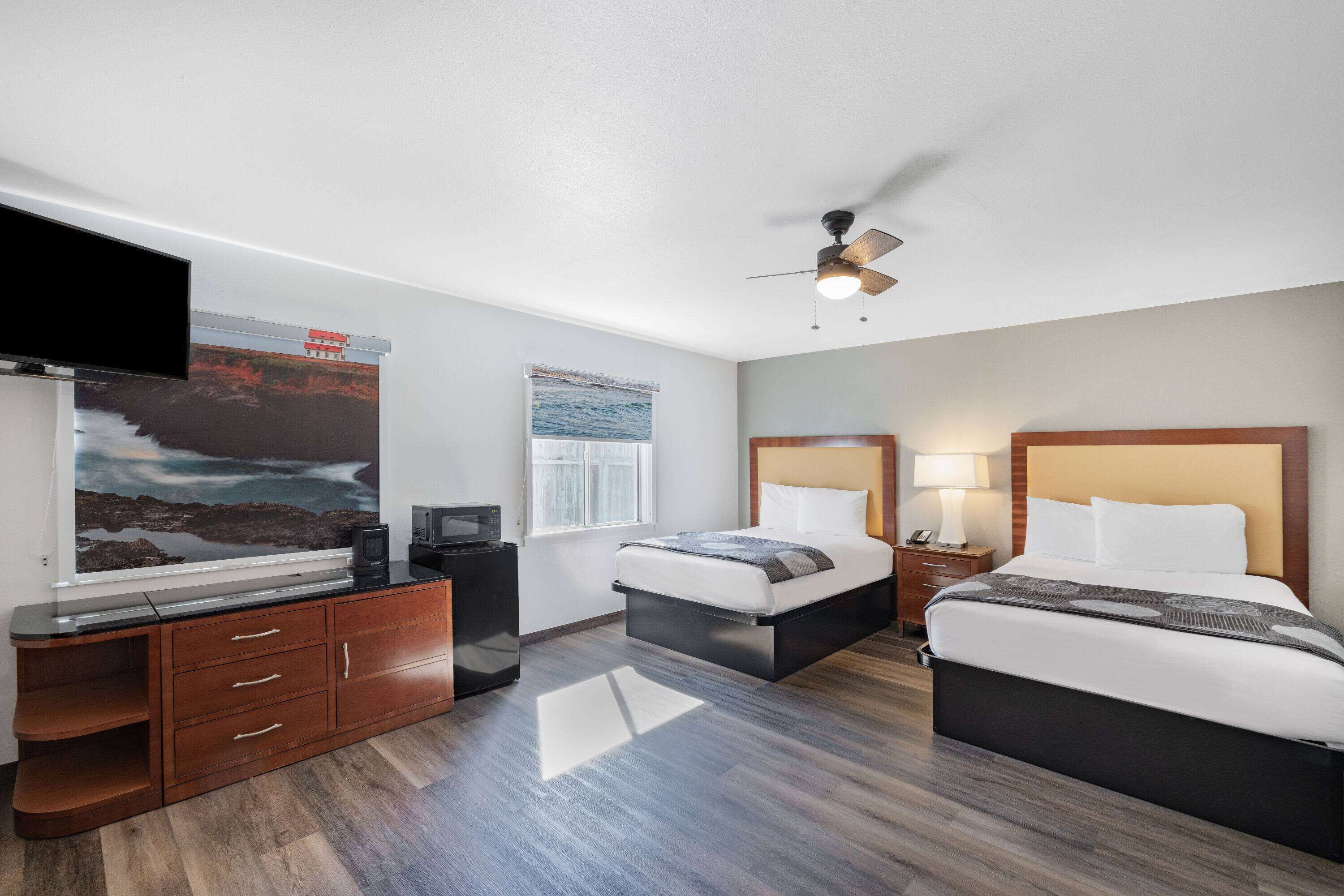 A hotel room with a bed, a desk, a TV, a ceiling fan, and artwork on the wall.