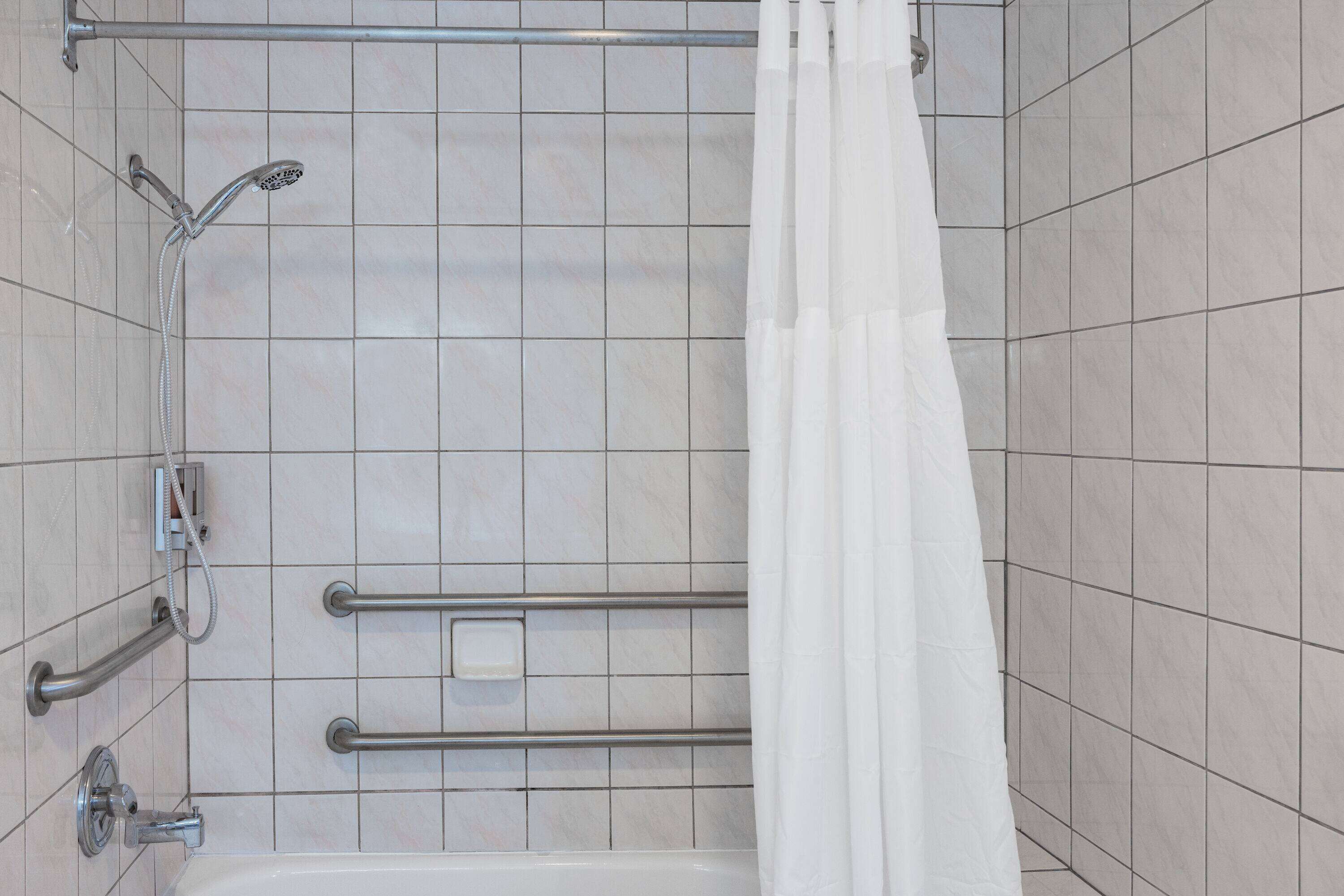 A shower area with a white bathtub, a handheld showerhead, and a grab bar.