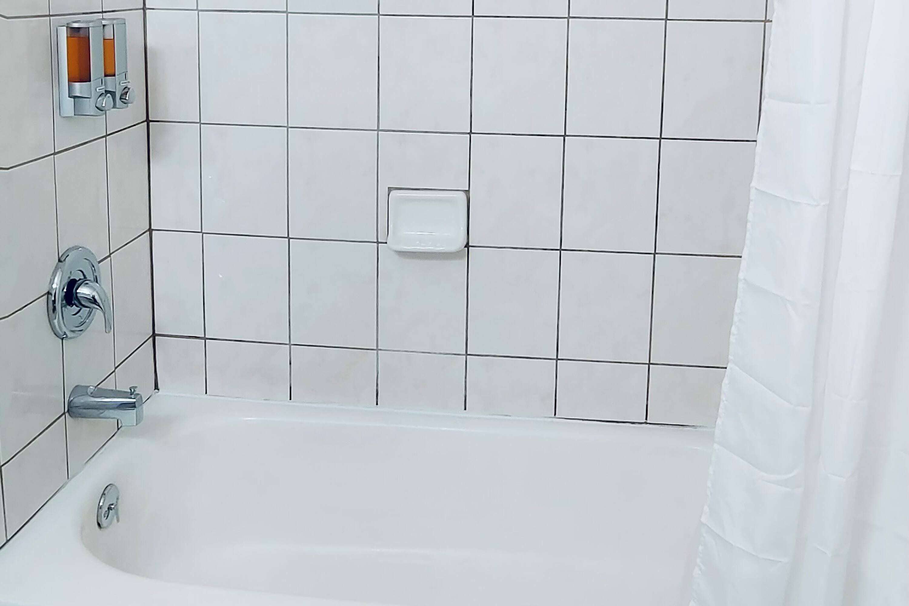 Un baño con una bañera blanca, grifería cromada y paredes de azulejos blancos.
