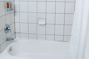Un baño con una bañera blanca, grifería cromada y paredes de azulejos blancos.