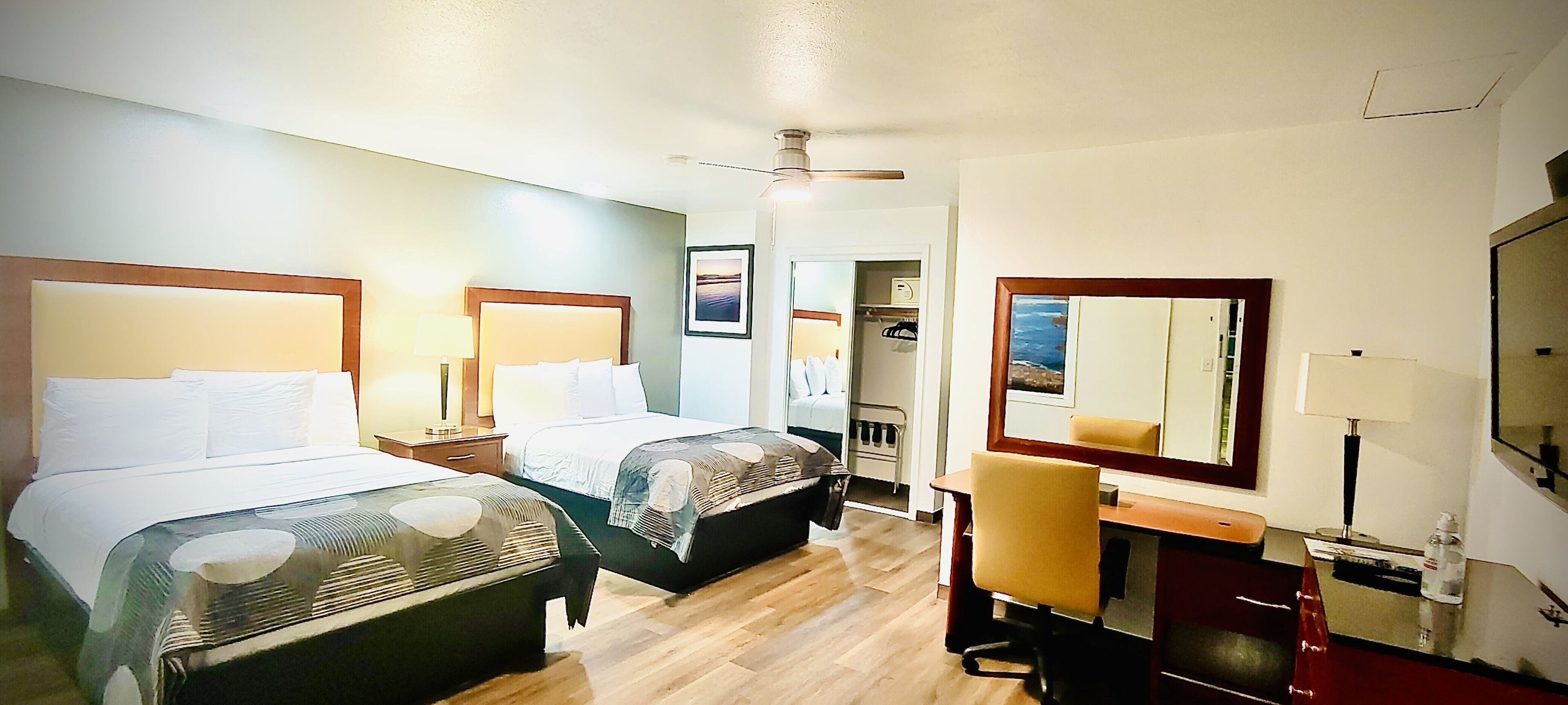 A hotel room with two beds, a desk, a chair, a mirror, and a wardrobe.