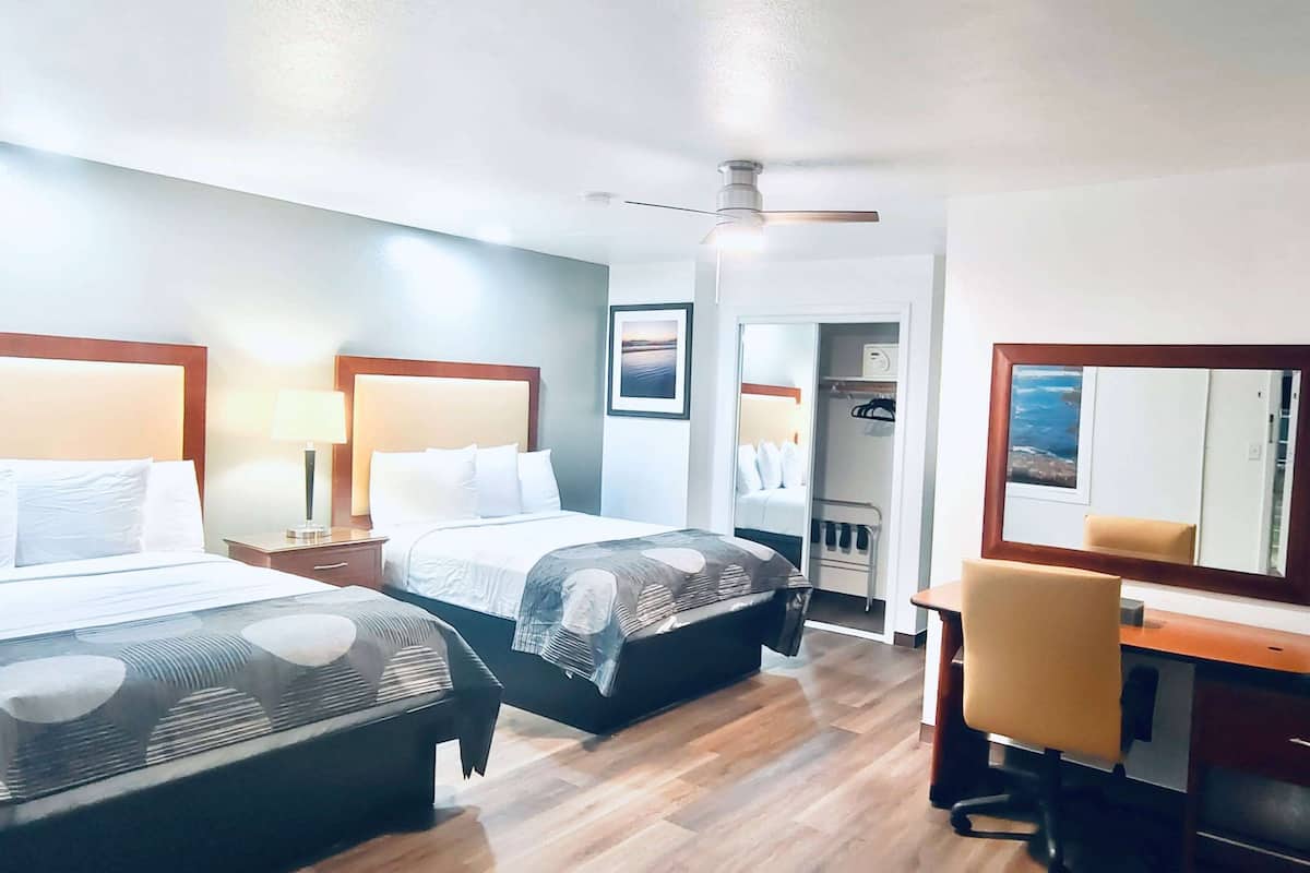 A hotel room with two beds, a desk, and a chair. There is a ceiling fan, a mirror, and a wardrobe.