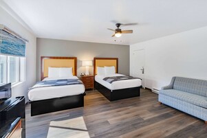 Una habitación de hotel con dos camas, un sofá, un ventilador de techo y una ventana con persianas.