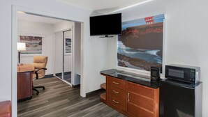 Ein Hotelzimmer mit Flachbildfernseher an der Wand, einer Mikrowelle in einem Schrank, einem Holztisch mit Stuhl und einem großen Fenster mit schöner Aussicht.