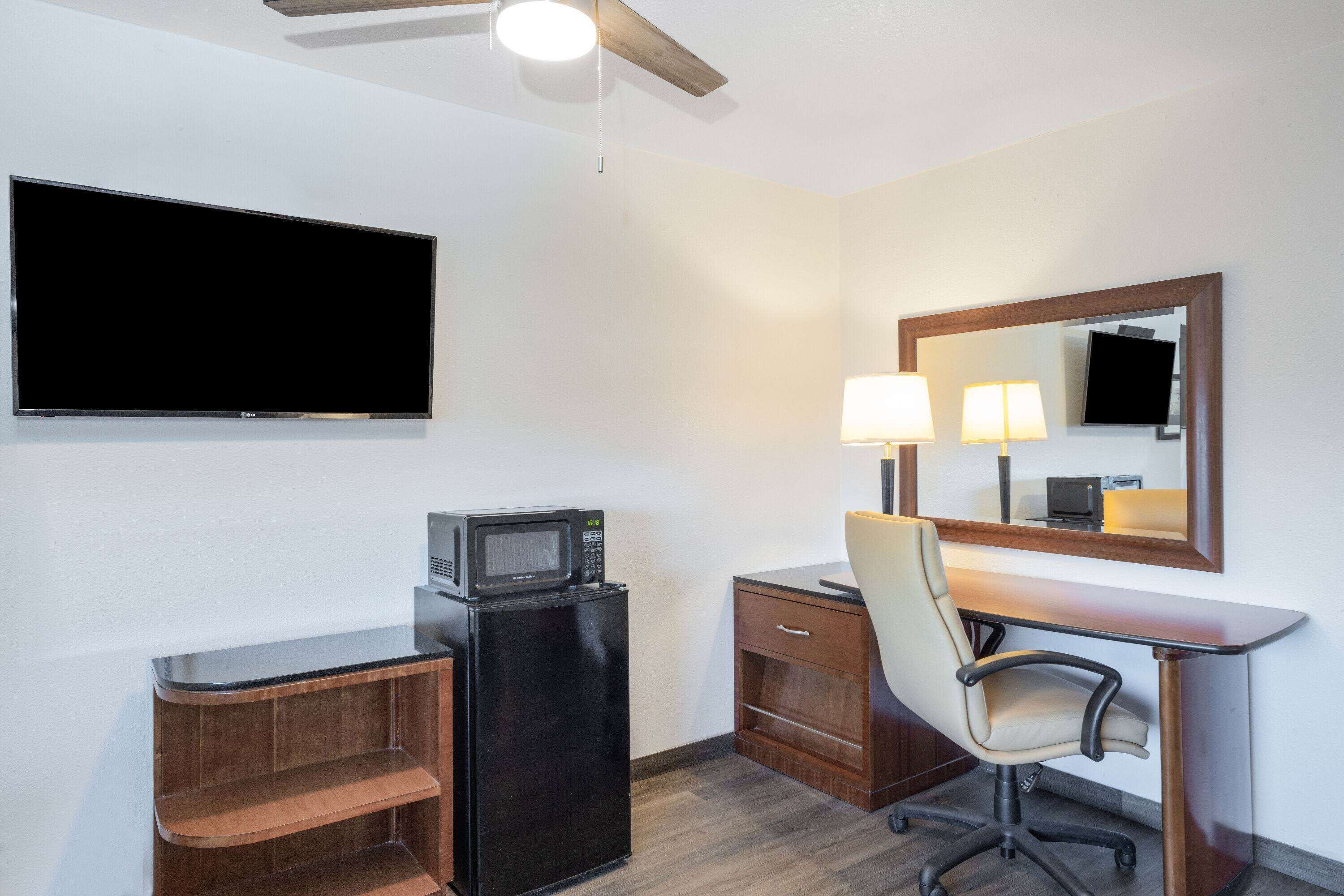 Habitación de hotel con televisor de pantalla plana, microondas, escritorio con silla, espejo y ventilador de techo.