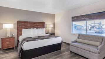 Habitación de hotel con una cama grande, una mesita de noche, una lámpara, un sofá y una ventana con vistas a la calle.