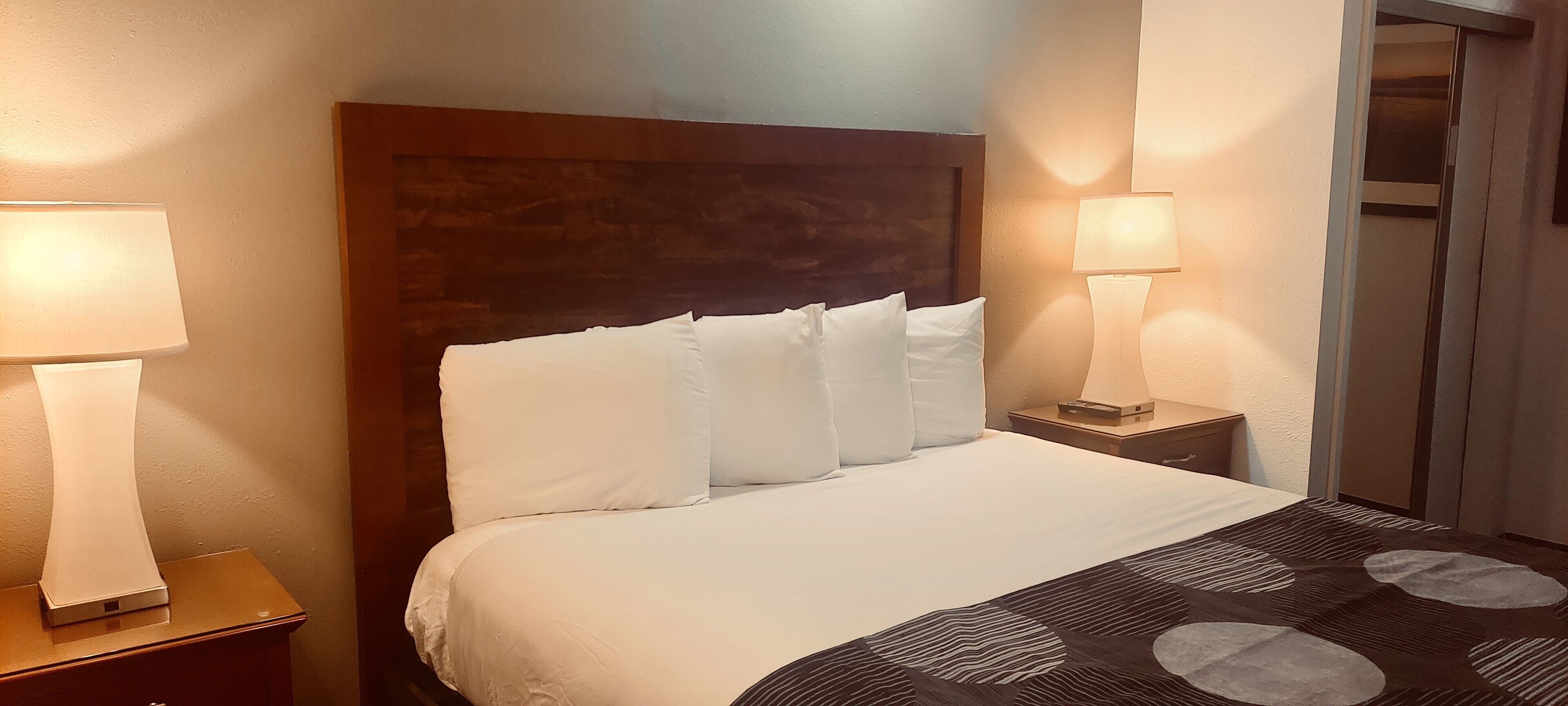 Una camera d'albergo con un letto grande, due abat-jour, una testiera in legno e un tappeto decorato.