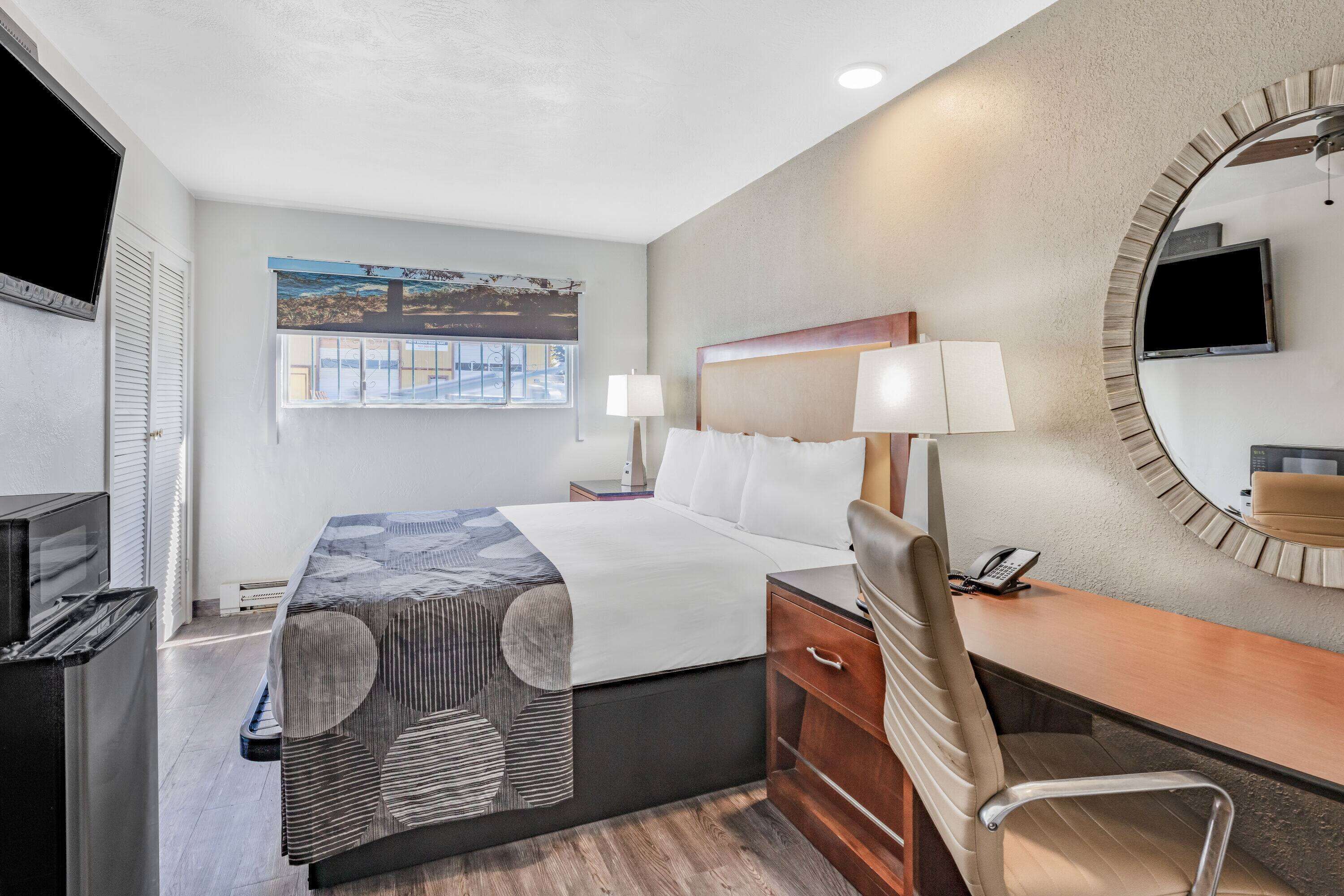 A hotel room with a bed, desk, chair, and a TV on the wall.