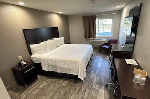 Habitación de hotel con una cama grande, un escritorio con computadora, una silla, televisor y una ventana con cortinas.