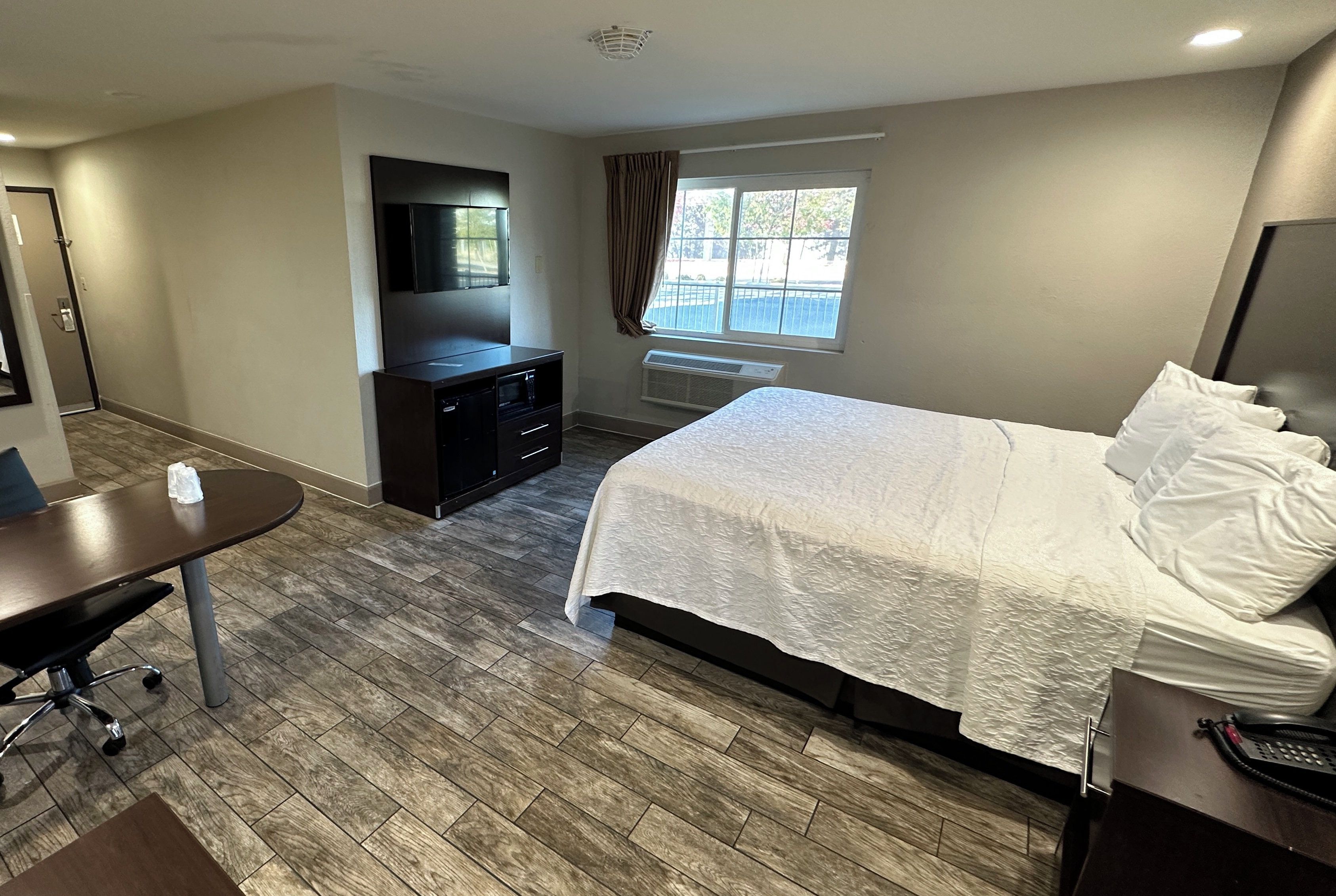 A hotel room with a bed, a desk, a TV, a window with curtains, and a heater.